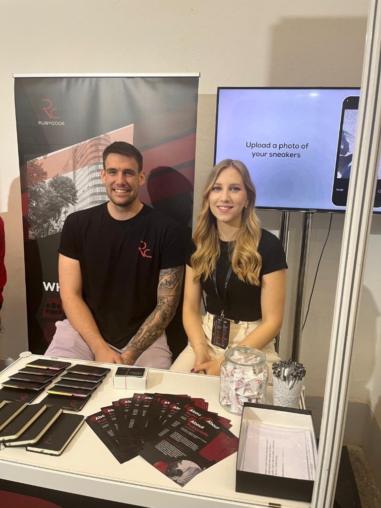 Two Rubycode team members at the company stand, with the Sneaker Finder app on screen